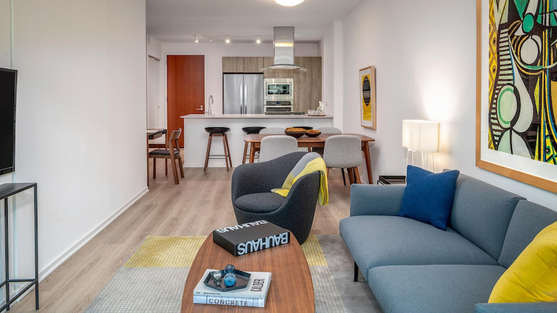 Cozy living room with gray sofa, bold artwork, and open kitchen with breakfast bar at Optima Signature apartments in downtown Chicago