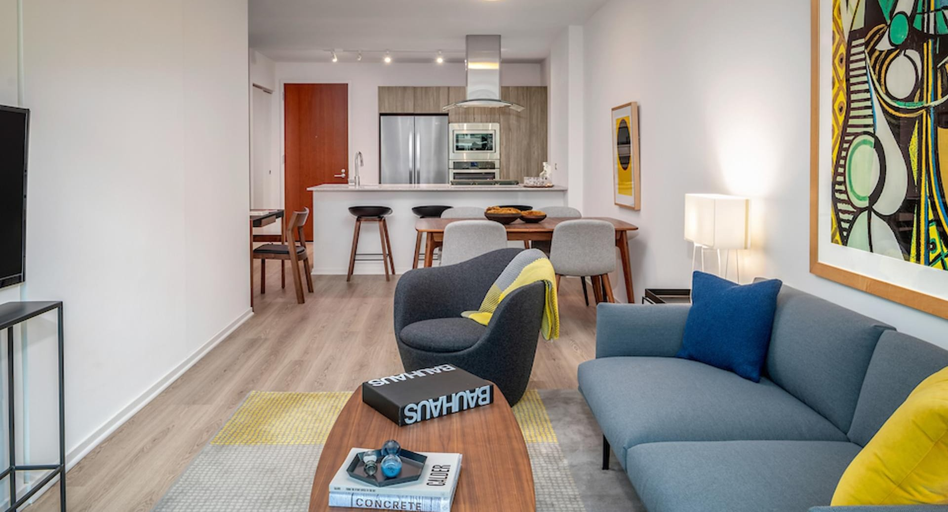 Cozy living room with gray sofa, bold artwork, and open kitchen with breakfast bar at Optima Signature apartments in downtown Chicago