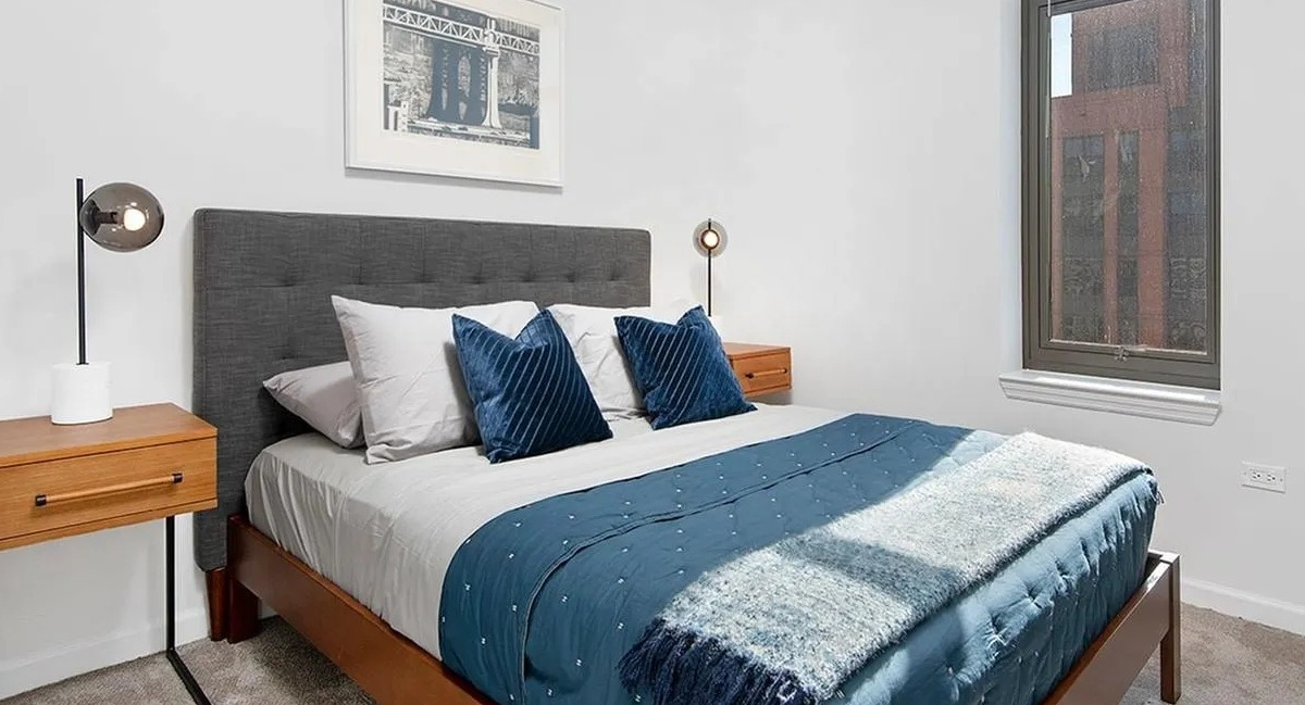Cozy bedroom with a queen-sized bed, two nightstands, and a large window bringing in natural light at Echelon at K Station in Chicago