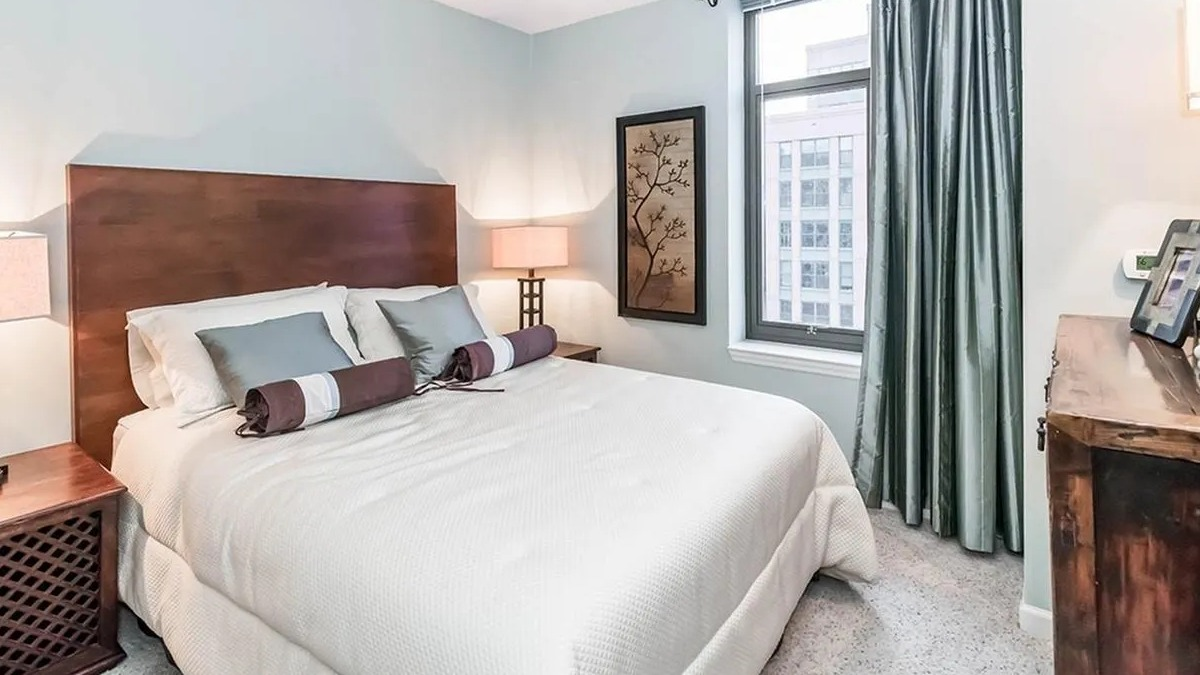 A cozy bedroom with a comfortable bed, warm wooden furniture, and a large window at Echelon at K Station in Chicago