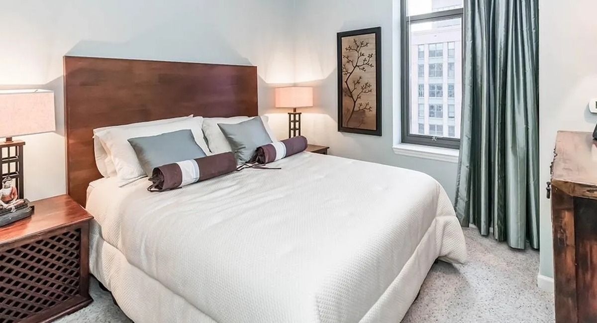A cozy bedroom with a comfortable bed, warm wooden furniture, and a large window at Echelon at K Station in Chicago