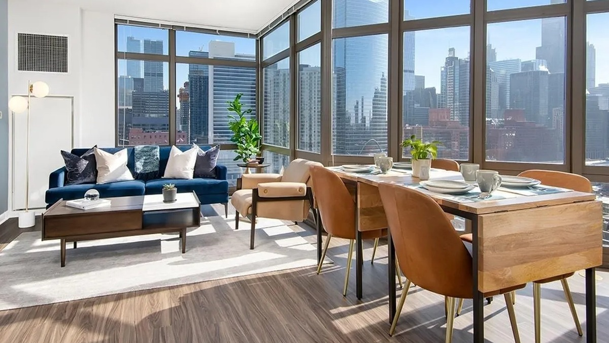 Bright living room with a blue sofa, modern dining table, and panoramic city views at Echelon at K Station in Chicago