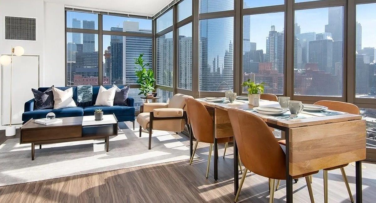 Bright living room with a blue sofa, modern dining table, and panoramic city views at Echelon at K Station in Chicago