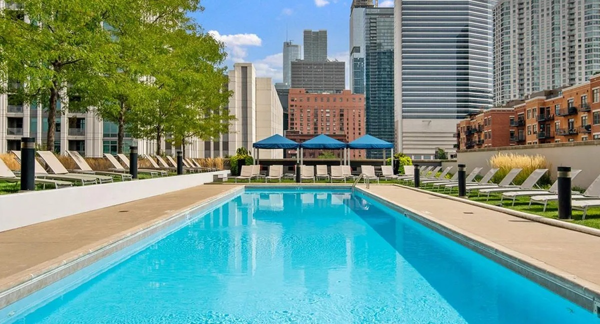 Sparkling outdoor swimming pool surrounded by lounge chairs with a vibrant city skyline backdrop at Echelon at K Station in Chicago