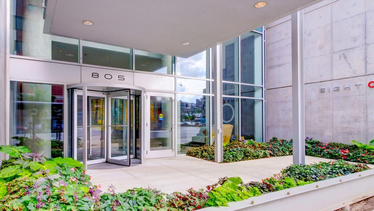 Modern building exterior of Eight O Five Apartments with a revolving glass door entrance and lush landscaping