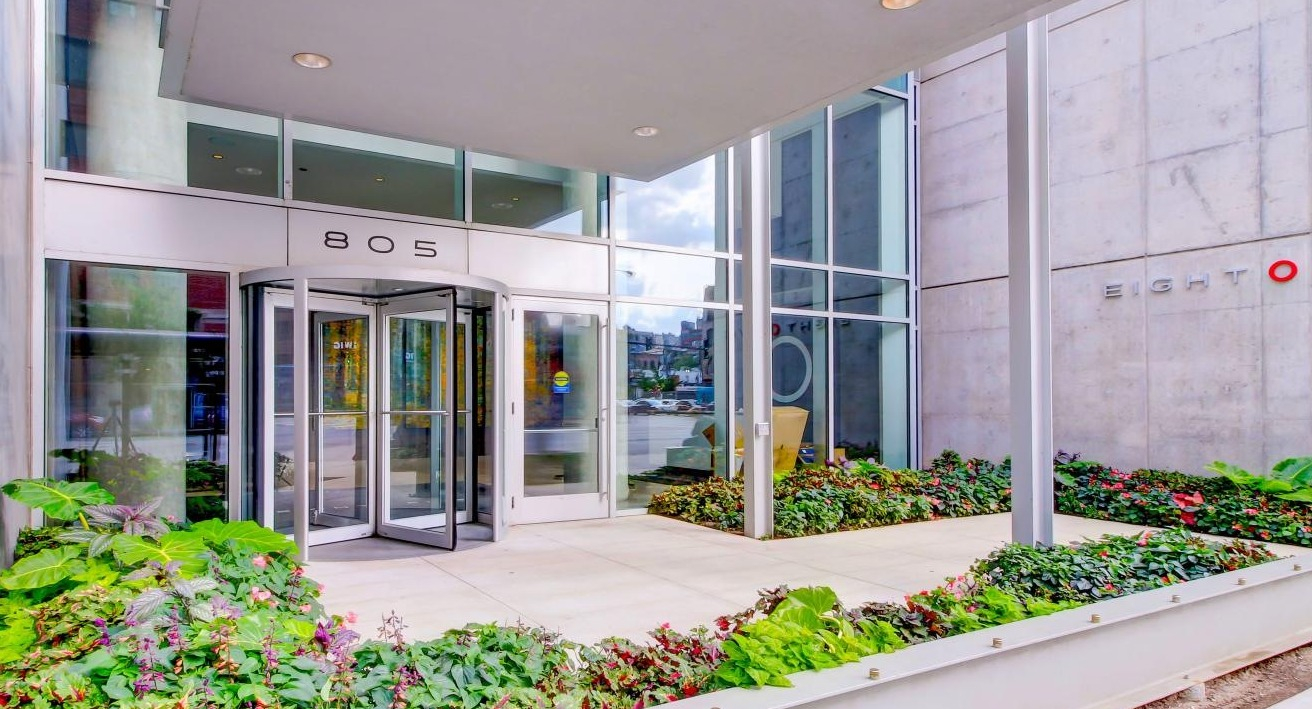 Modern building exterior of Eight O Five Apartments with a revolving glass door entrance and lush landscaping