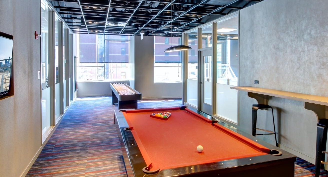 Vibrant game room with a pool table, shuffleboard, and bar seating, perfect for entertainment at Eight O Five Apartments in Chicago