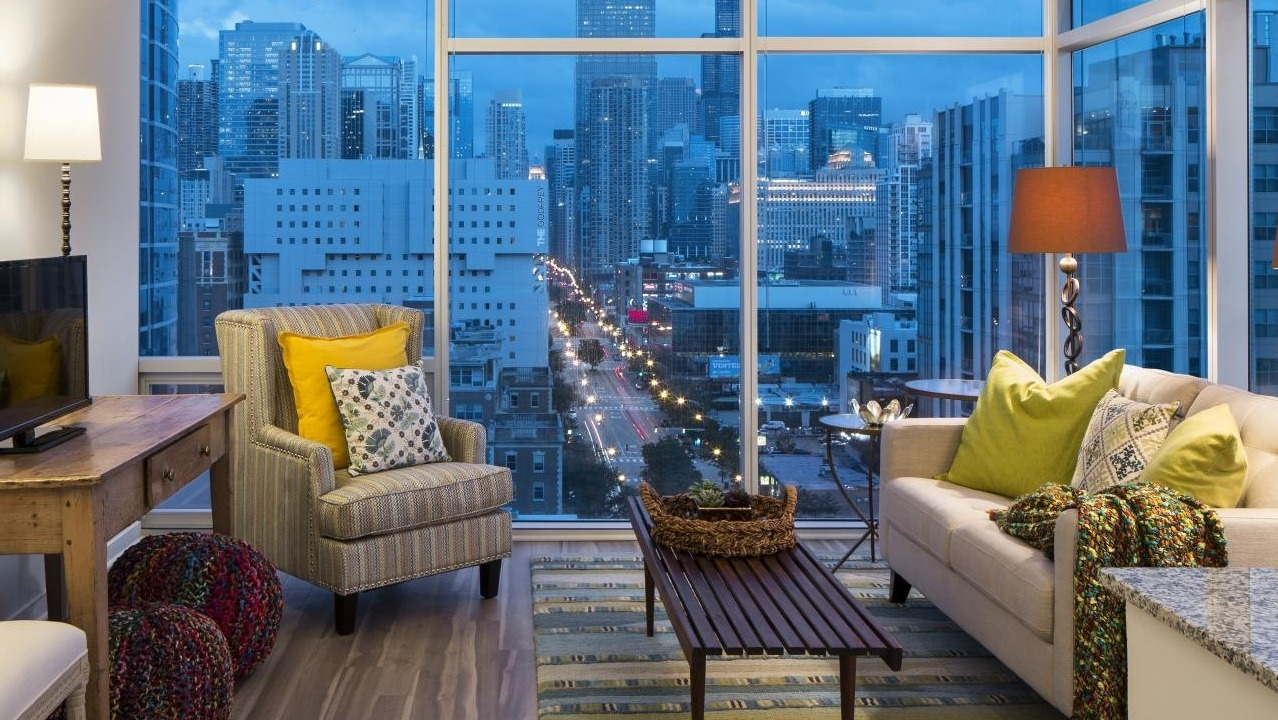 Modern apartment living room with cozy couch, accent chairs, and floor-to-ceiling windows showing Chicago city views at Eight O Five Apartments in Chicago