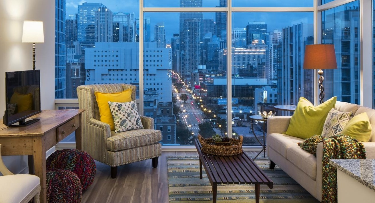 Modern apartment living room with cozy couch, accent chairs, and floor-to-ceiling windows showing Chicago city views at Eight O Five Apartments in Chicago
