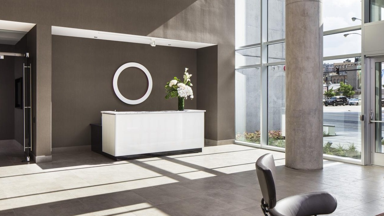 Modern apartment lobby with a sleek white reception desk, large ring art, and floor-to-ceiling windows at Eight O Five Apartments in Chicago