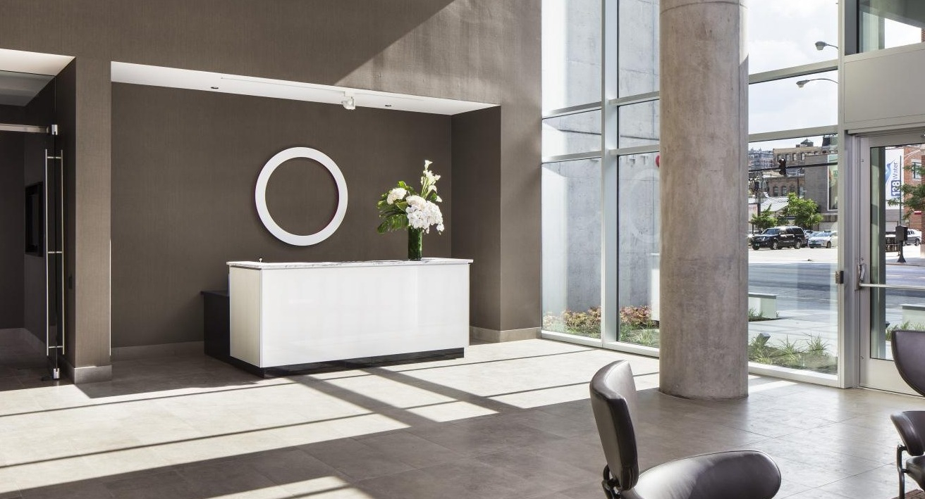 Modern apartment lobby with a sleek white reception desk, large ring art, and floor-to-ceiling windows at Eight O Five Apartments in Chicago