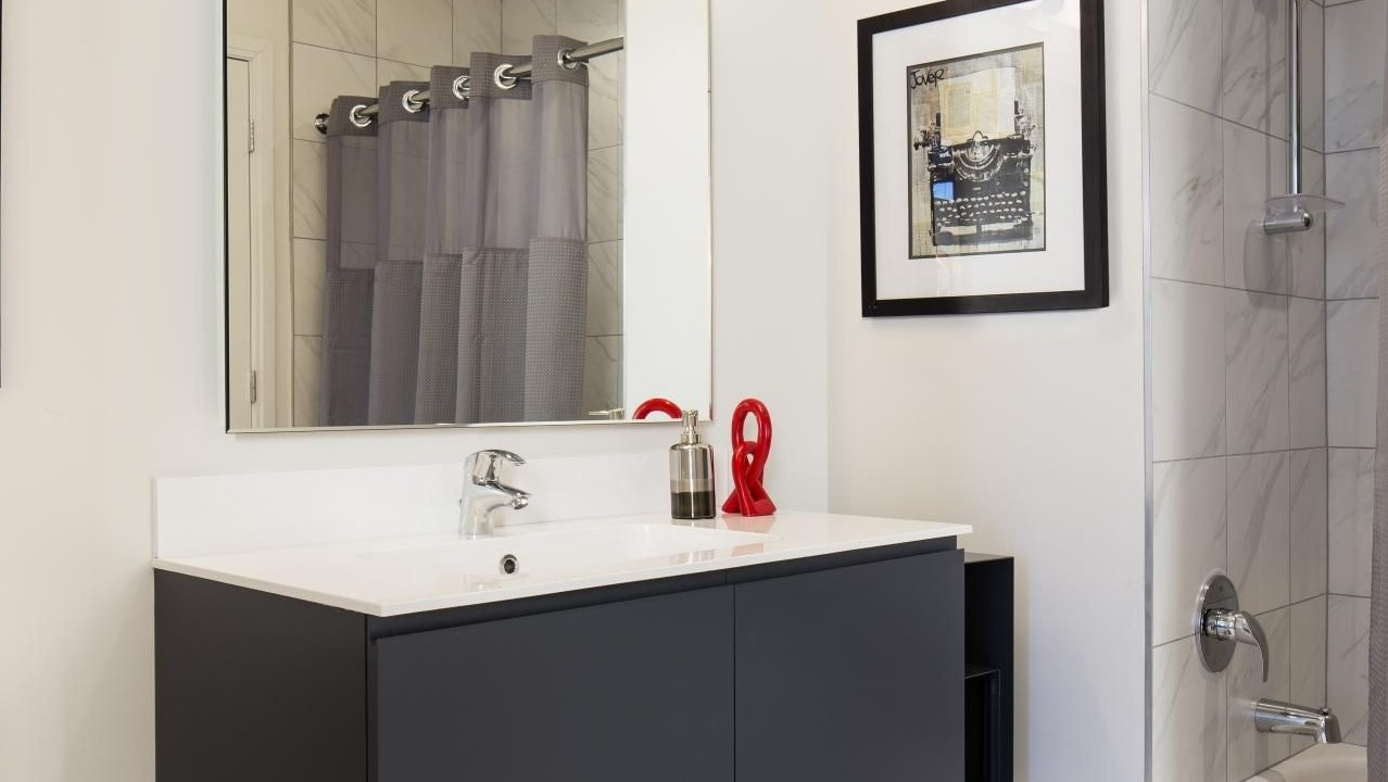 Sleek, modern bathroom with a dark vanity, white counter, large mirror, and shower with gray curtain at Eight O Five Apartments in Chicago