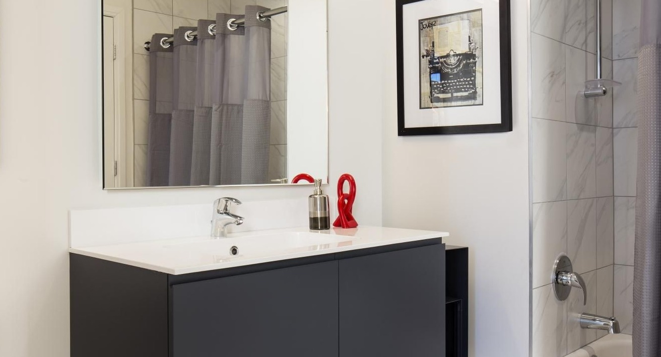Sleek, modern bathroom with a dark vanity, white counter, large mirror, and shower with gray curtain at Eight O Five Apartments in Chicago
