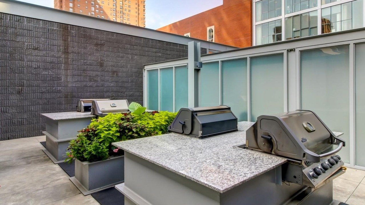 Outdoor grilling area with multiple modern barbecues and prep counters, surrounded by urban landscaping at Eight O Five Apartments in Chicago