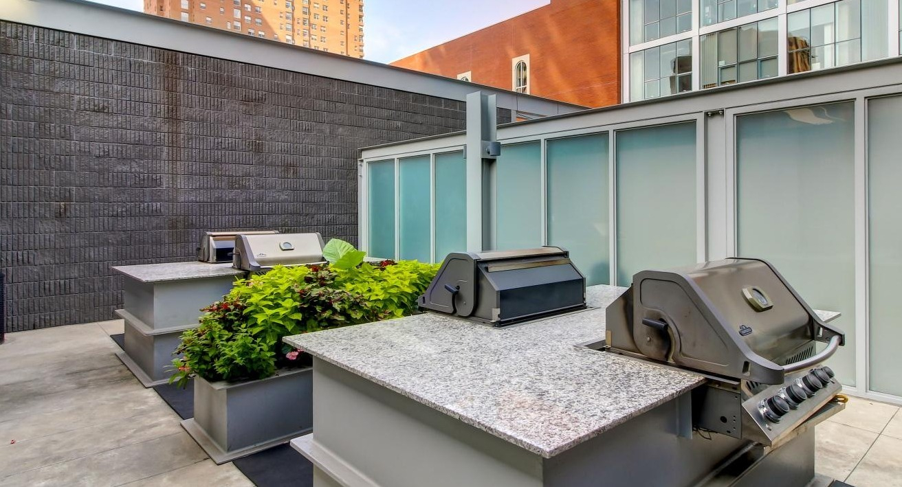 Outdoor grilling area with multiple modern barbecues and prep counters, surrounded by urban landscaping at Eight O Five Apartments in Chicago