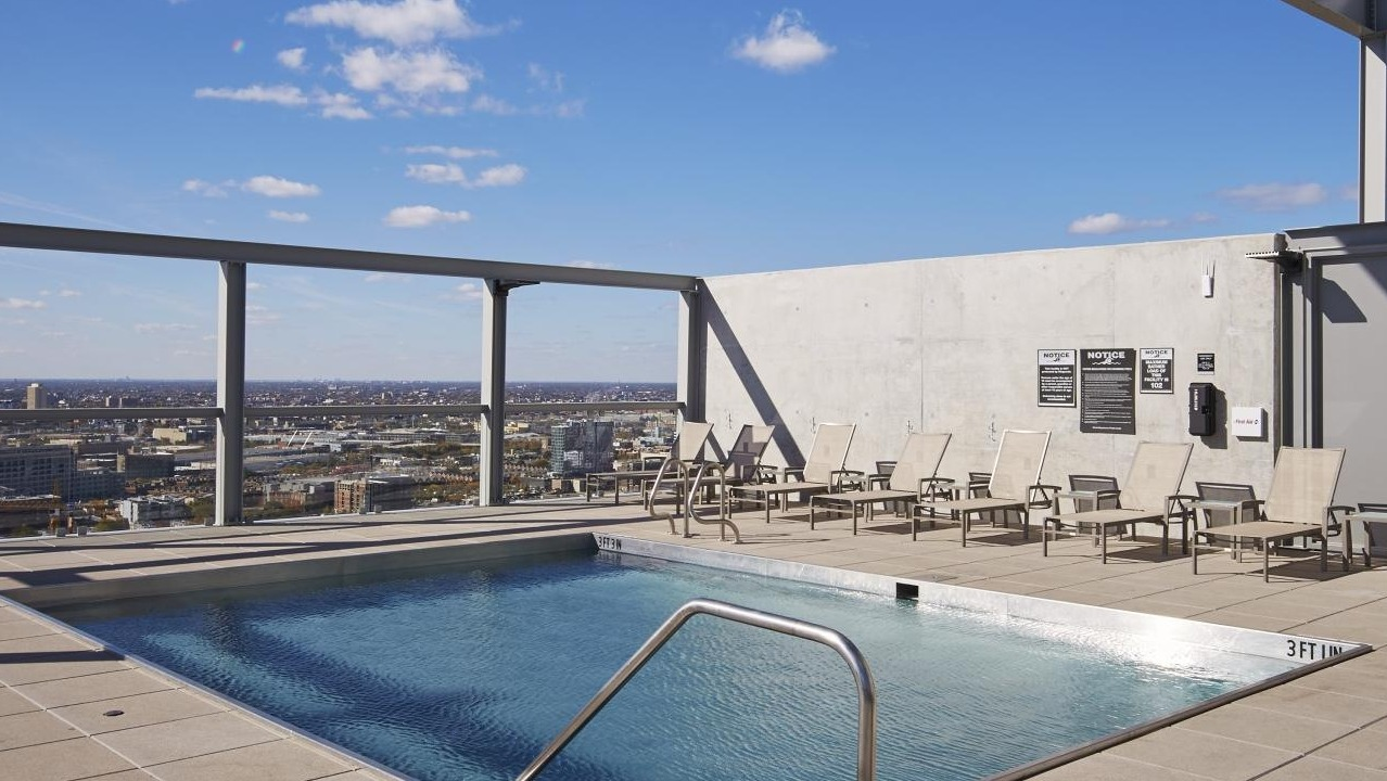 Serene rooftop swimming pool with lounge chairs, offering stunning panoramic views of the city skyline at Eight O Five Apartments in Chicago