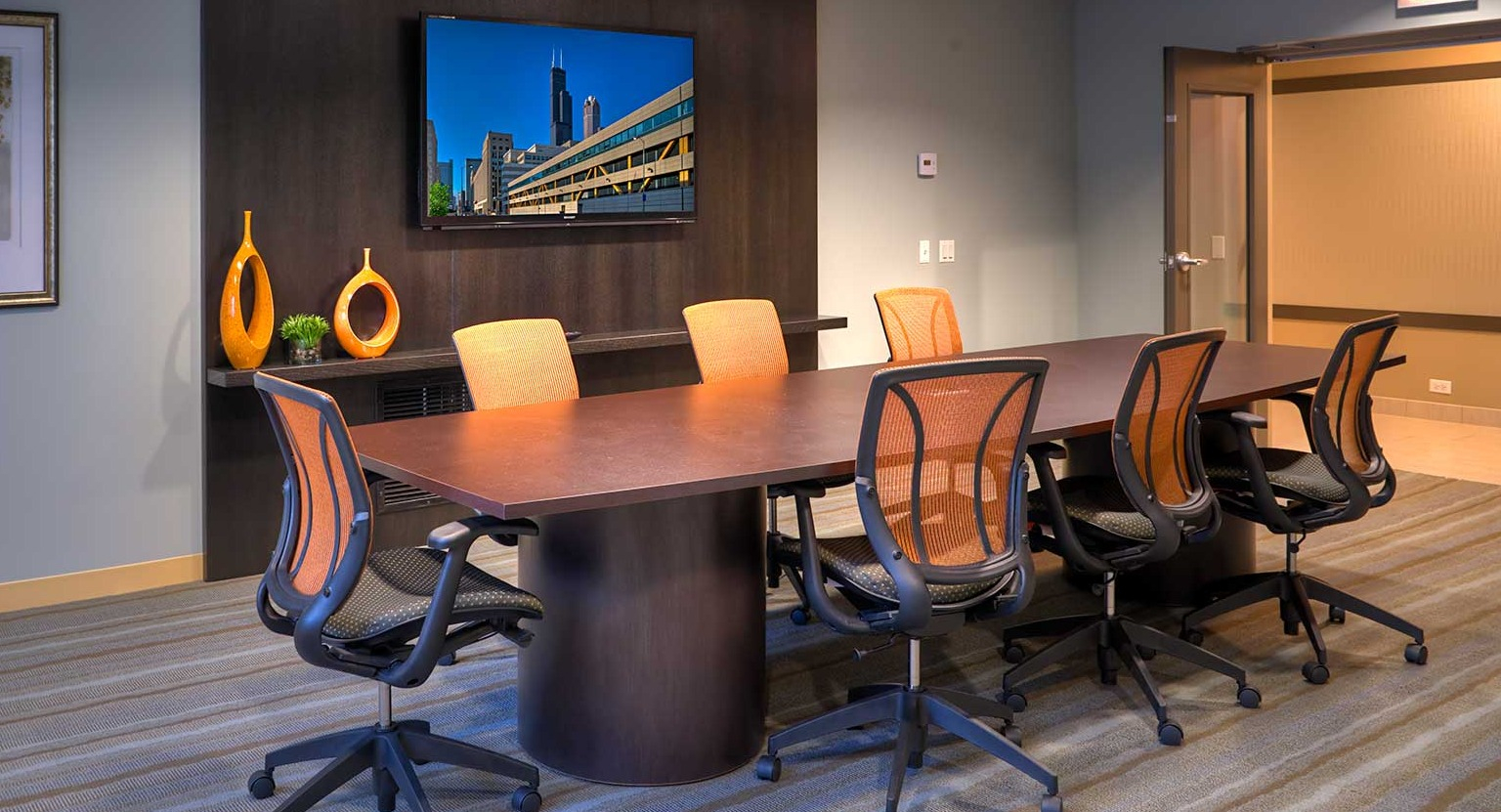 Modern conference room with a large table, ergonomic chairs, and a wall-mounted TV for meetings at Eleven Thirty apartments in Chicago