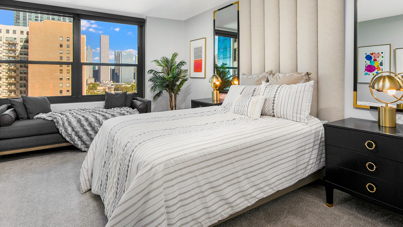 Luxurious bedroom with a padded headboard, stylish bedding, comfortable seating, and large windows offering city views at Eleven Thirty in Chicago