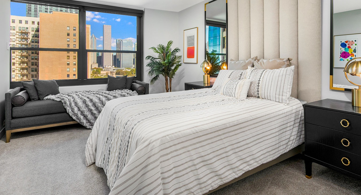 Luxurious bedroom with a padded headboard, stylish bedding, comfortable seating, and large windows offering city views at Eleven Thirty in Chicago