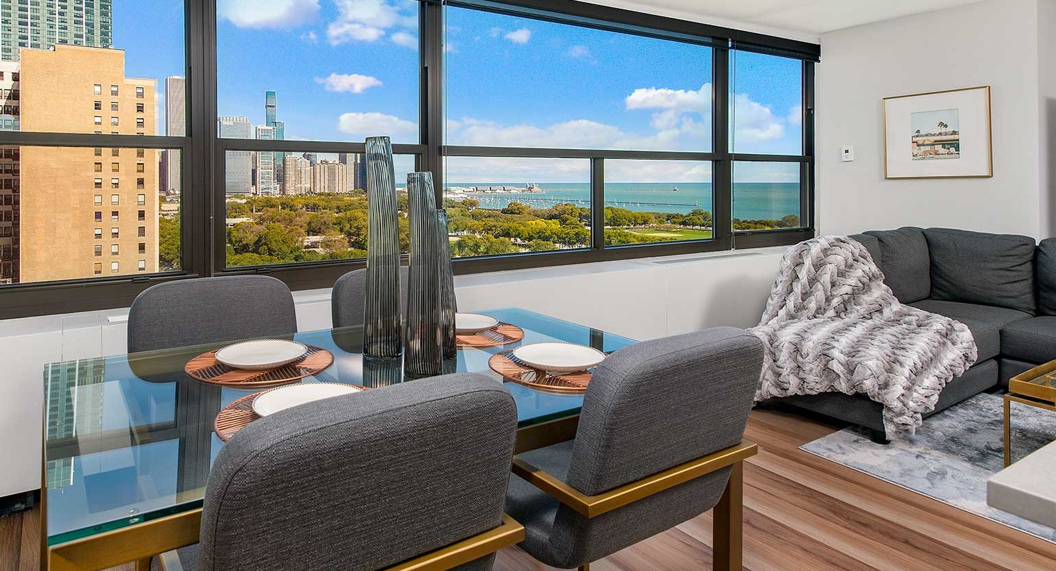 Elegant dining room with a glass table and upholstered chairs, offering stunning lake and city views at Eleven Thirty apartments in Chicago