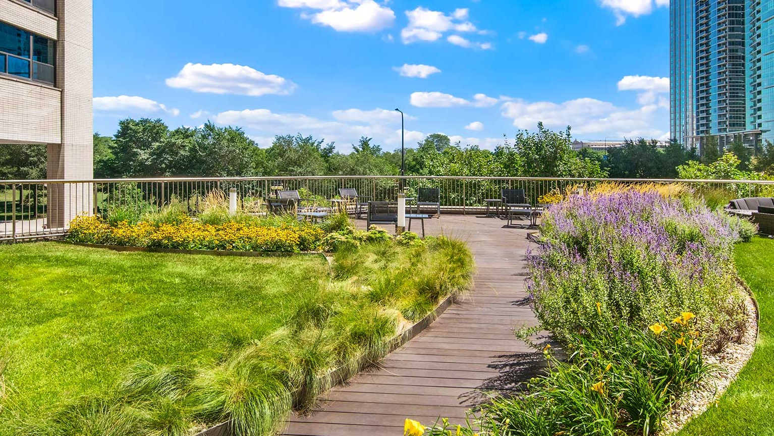 Beautifully landscaped outdoor courtyard with a winding wooden path, lush greenery, and comfortable seating areas at Eleven Thirty in Chicago