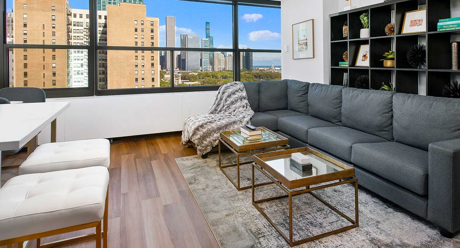 Elegant living room featuring a large sectional sofa, shelving, and expansive windows offering panoramic city views at Eleven Thirty in Chicago