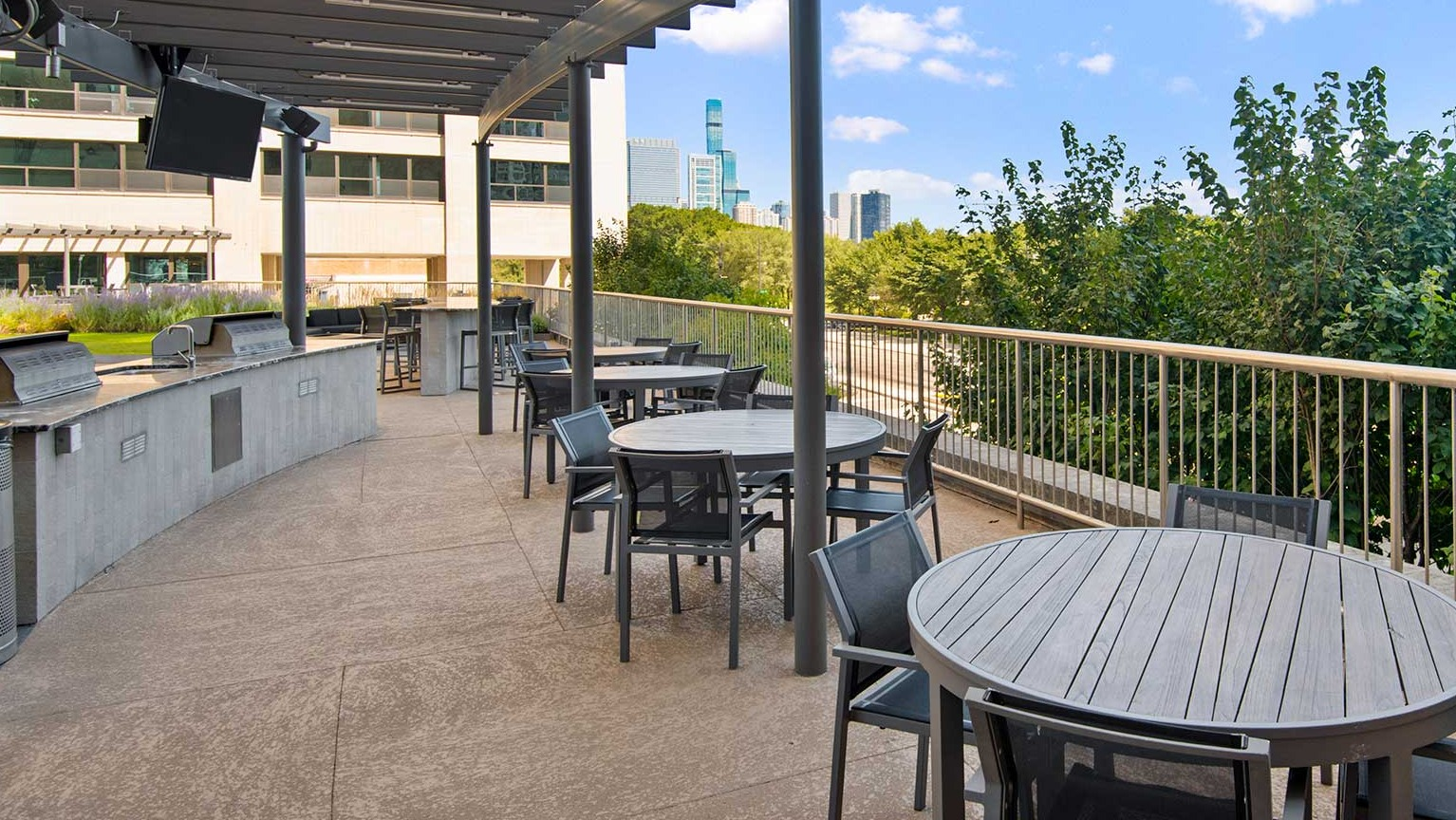 Spacious outdoor dining area with tables, chairs, and integrated BBQ grills under a pergola, at Eleven Thirty apartments in Chicago
