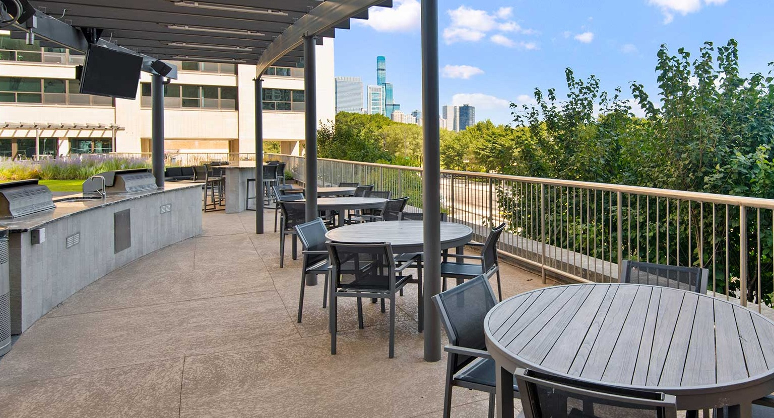 Spacious outdoor dining area with tables, chairs, and integrated BBQ grills under a pergola, at Eleven Thirty apartments in Chicago