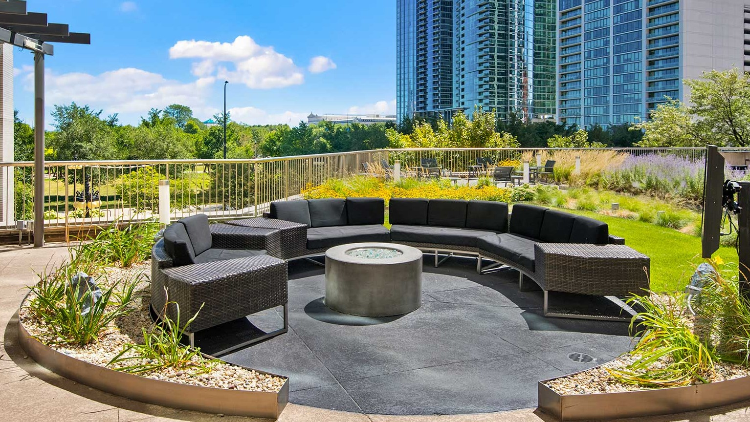 Inviting outdoor lounge area with circular seating and a modern fire pit, surrounded by greenery and city views at Eleven Thirty in Chicago