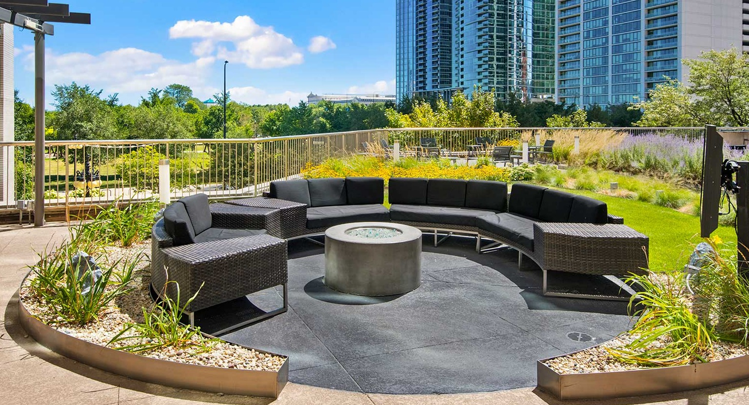 Inviting outdoor lounge area with circular seating and a modern fire pit, surrounded by greenery and city views at Eleven Thirty in Chicago