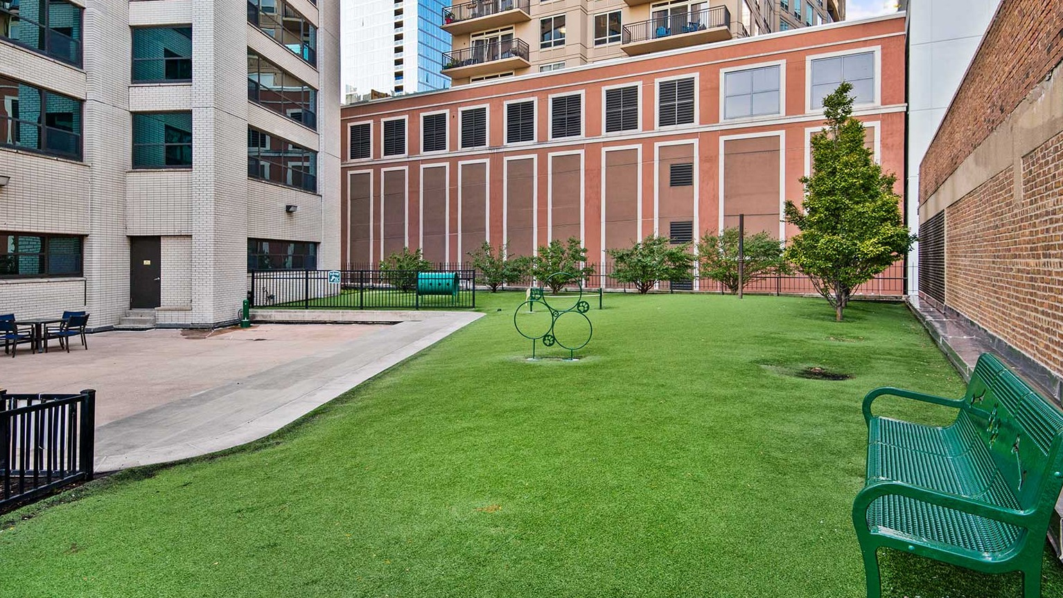 Outdoor pet relief area with artificial turf, benches, and fencing, surrounded by apartment buildings at Eleven Thirty in Chicago