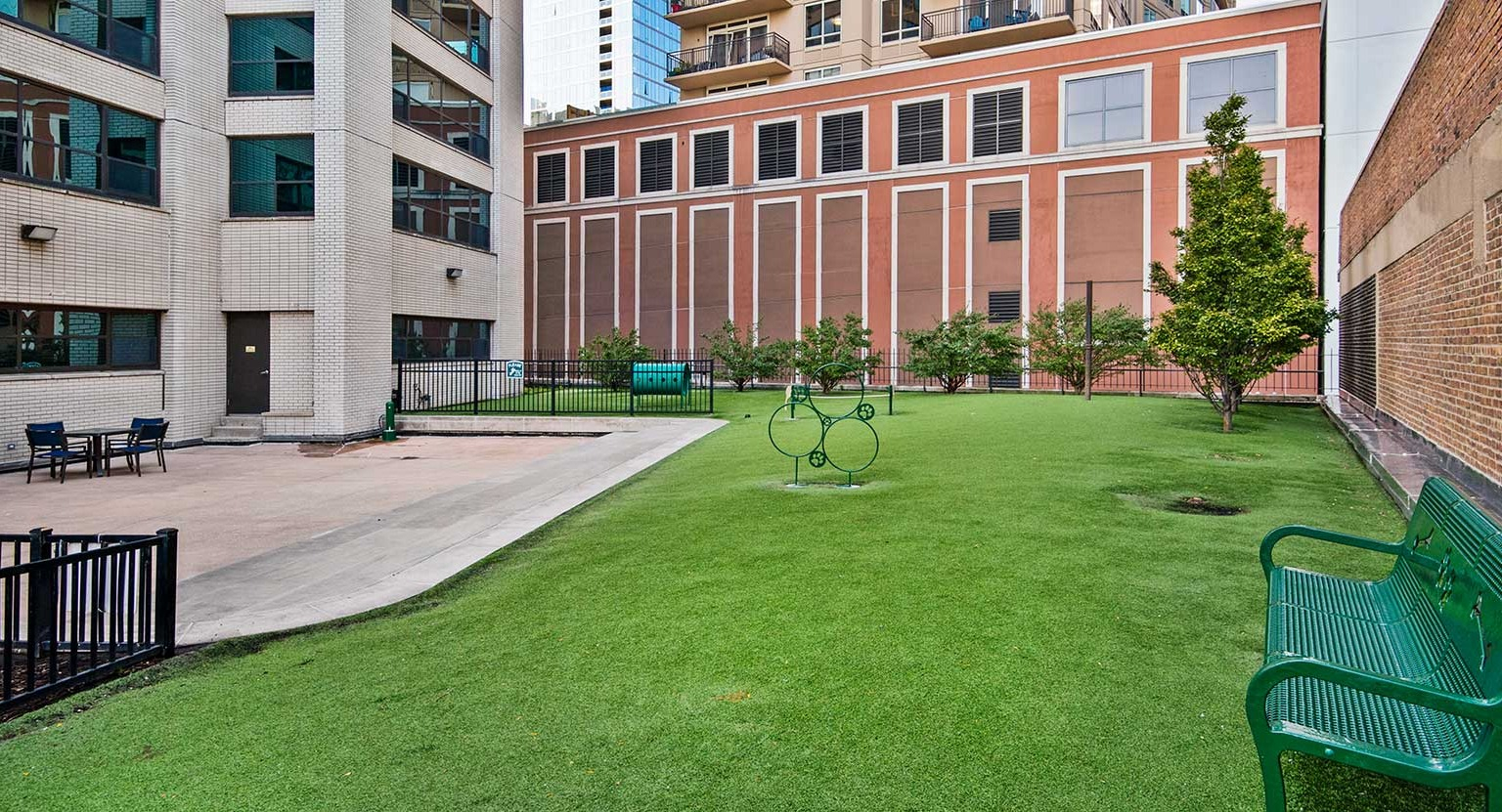 Outdoor pet relief area with artificial turf, benches, and fencing, surrounded by apartment buildings at Eleven Thirty in Chicago
