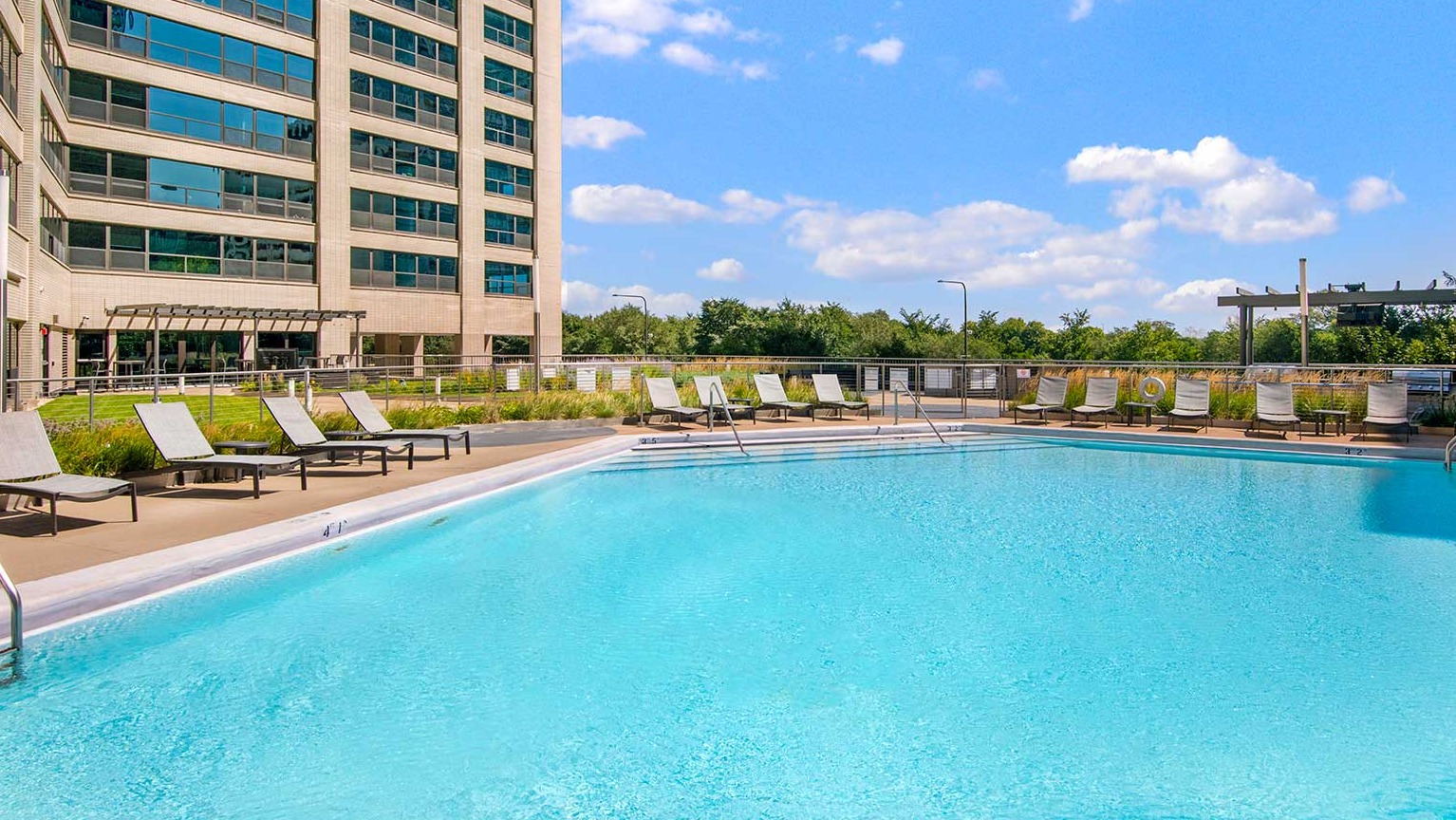 Large outdoor swimming pool surrounded by lounge chairs and a high-rise building backdrop, at Eleven Thirty apartments in Chicago