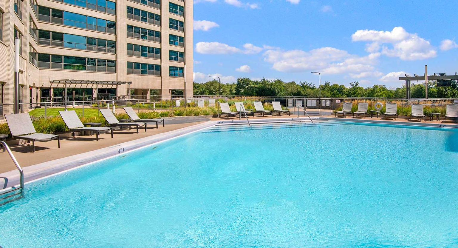 Large outdoor swimming pool surrounded by lounge chairs and a high-rise building backdrop, at Eleven Thirty apartments in Chicago