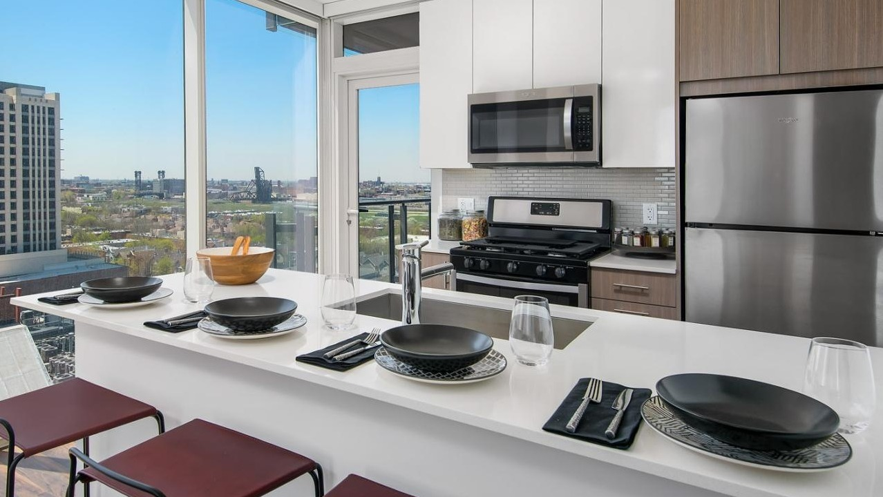 Modern apartment kitchen with a large island for dining, stainless steel appliances, and expansive city views at Eleven40 in Chicago