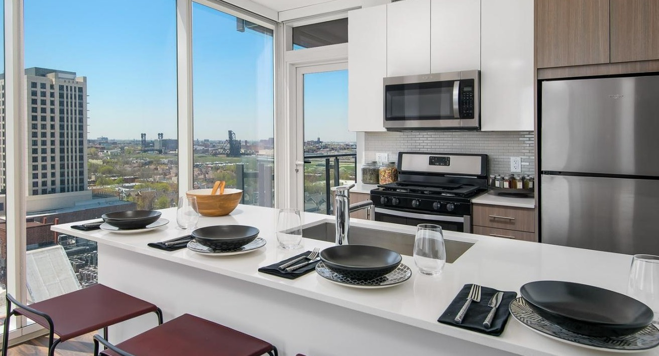 Modern apartment kitchen with a large island for dining, stainless steel appliances, and expansive city views at Eleven40 in Chicago