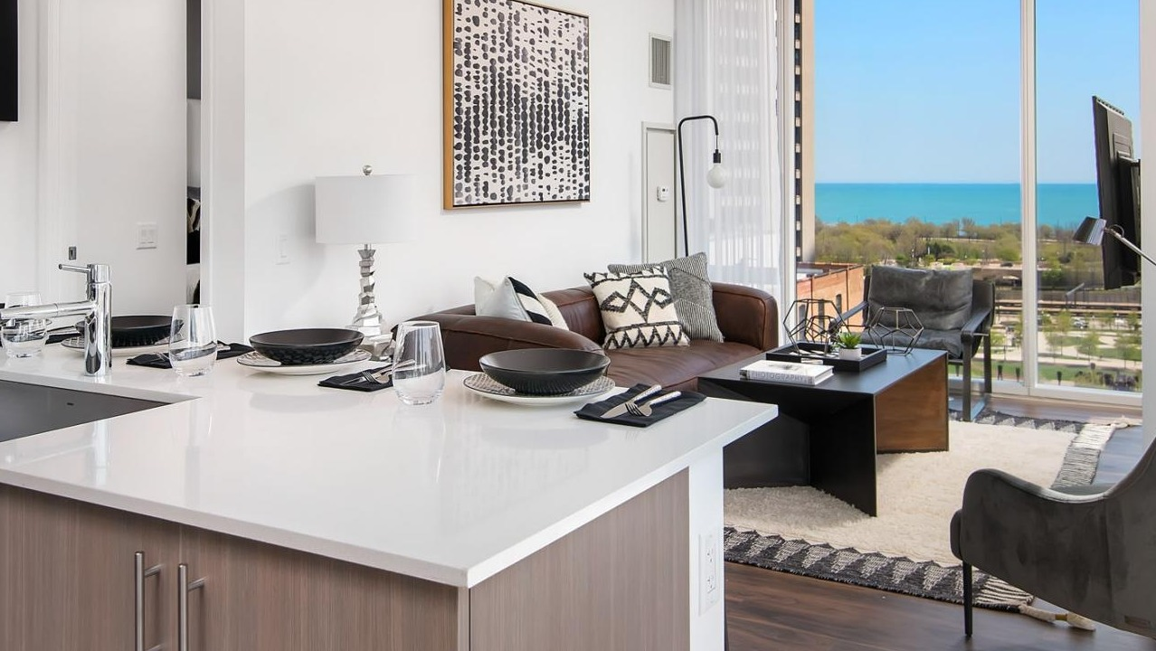 Modern apartment kitchen with a dining island, flowing into a living room with expansive windows showcasing lake views at Eleven40 in Chicago