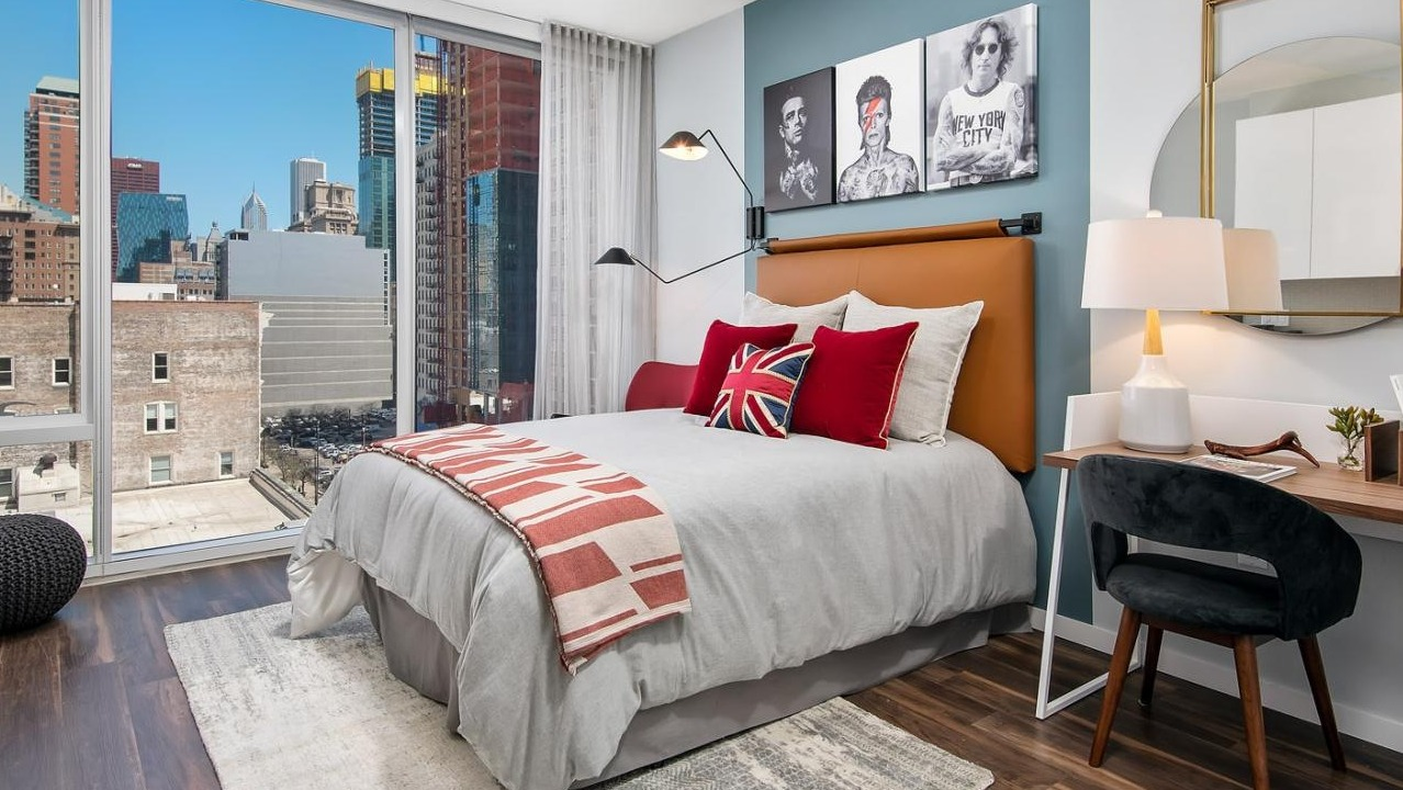 Stylish apartment bedroom with a comfortable bed, a dedicated work desk, and large windows showcasing city views at Eleven40 in Chicago