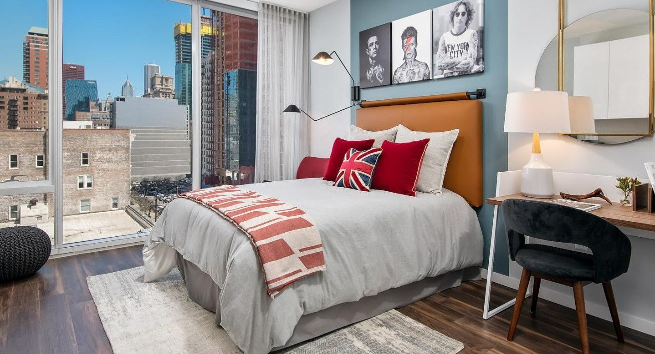 Stylish apartment bedroom with a comfortable bed, a dedicated work desk, and large windows showcasing city views at Eleven40 in Chicago
