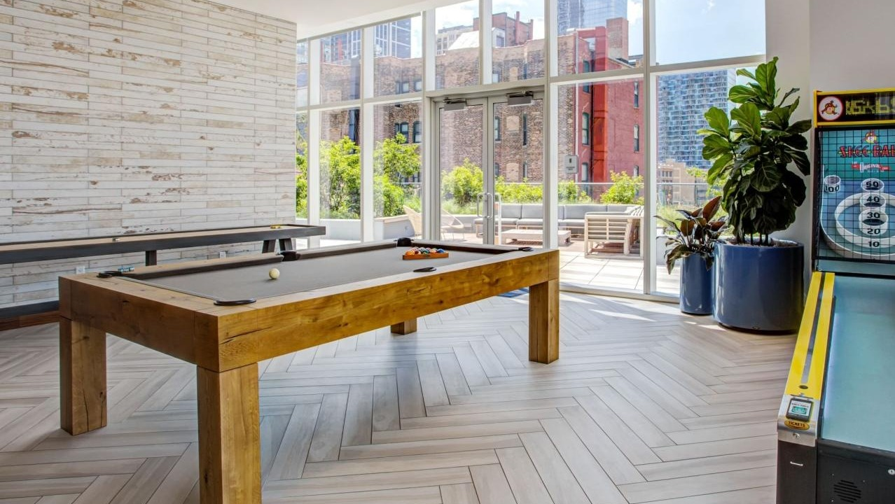 Fun-filled game room featuring a billiards table, shuffleboard, and an arcade game, with access to an outdoor patio at Eleven40 in Chicago