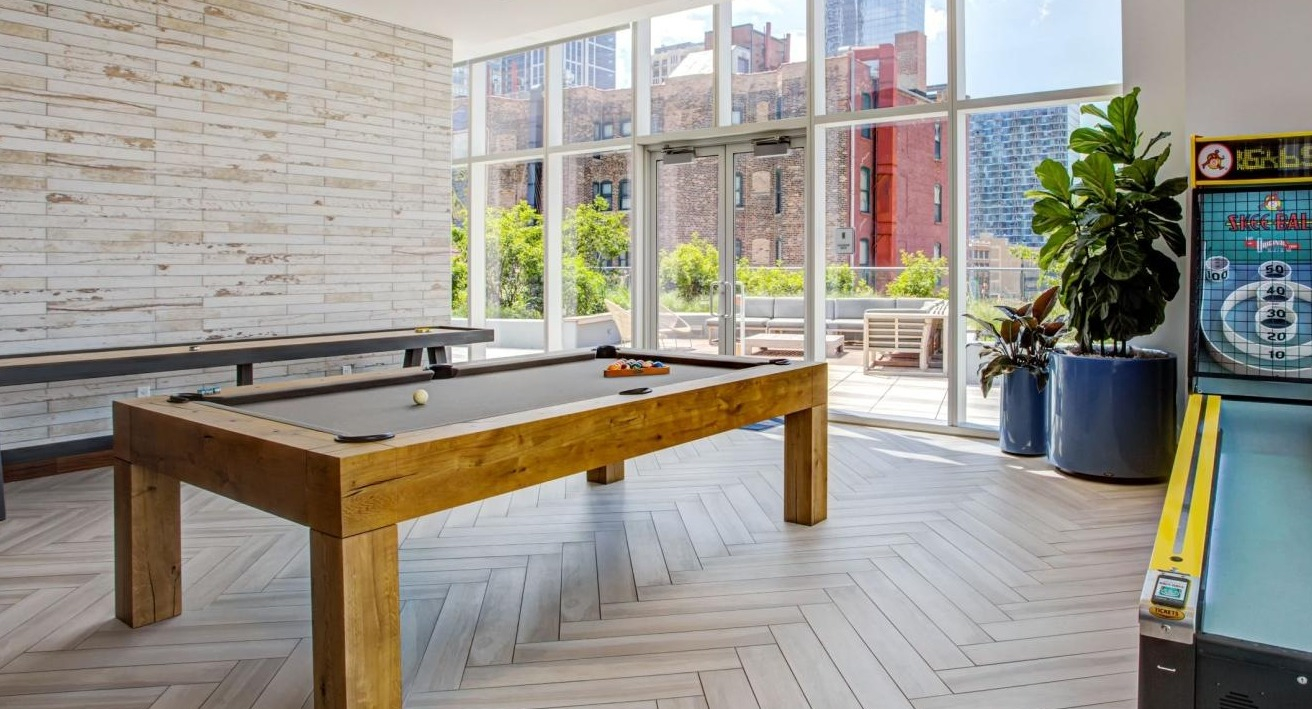 Fun-filled game room featuring a billiards table, shuffleboard, and an arcade game, with access to an outdoor patio at Eleven40 in Chicago
