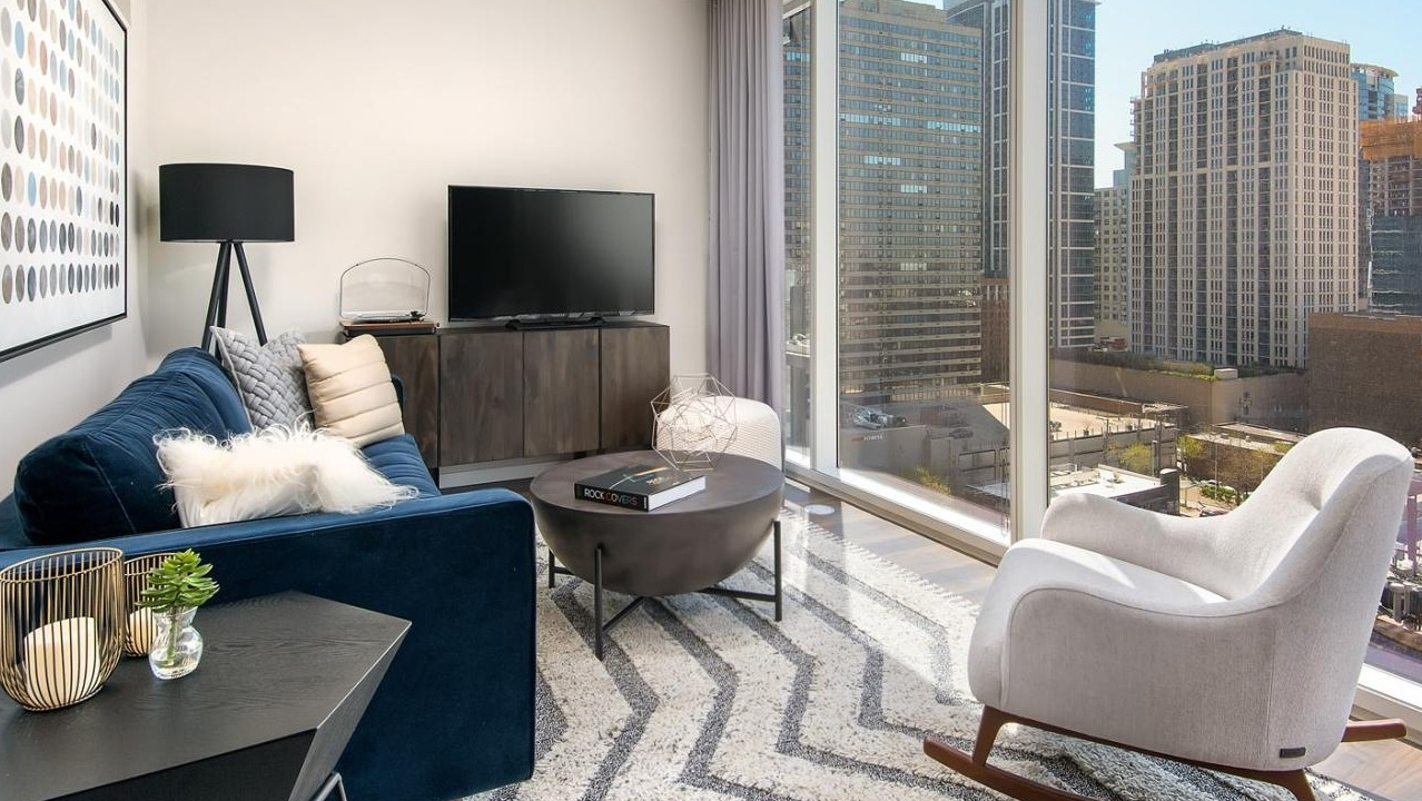Inviting apartment living room with a blue sofa, modern decor, and floor-to-ceiling windows offering expansive cityscape views at Eleven40 in Chicago