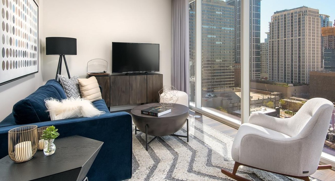 Inviting apartment living room with a blue sofa, modern decor, and floor-to-ceiling windows offering expansive cityscape views at Eleven40 in Chicago