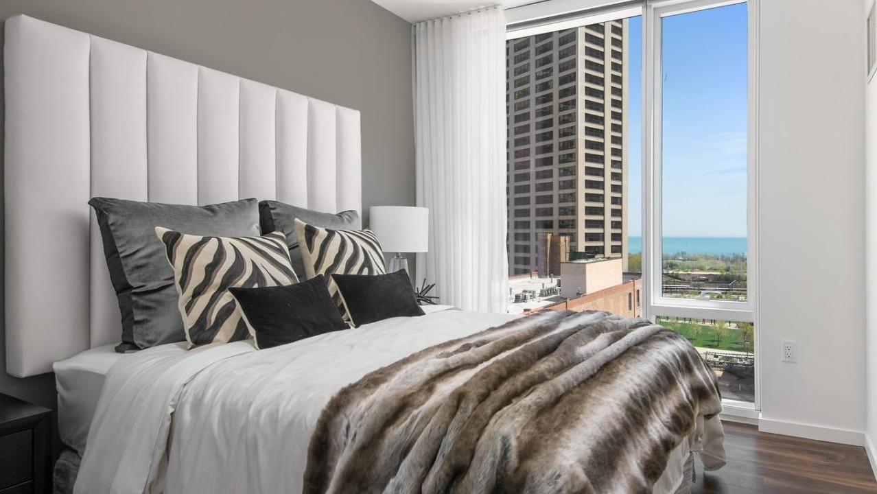Luxurious master bedroom featuring a plush bed, sophisticated decor, and large windows offering lake views at Eleven40 apartments in Chicago