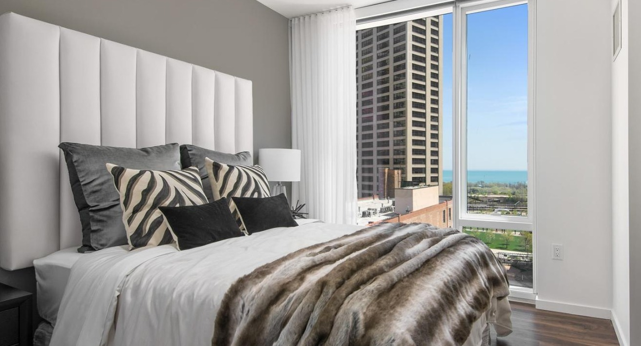 Luxurious master bedroom featuring a plush bed, sophisticated decor, and large windows offering lake views at Eleven40 apartments in Chicago