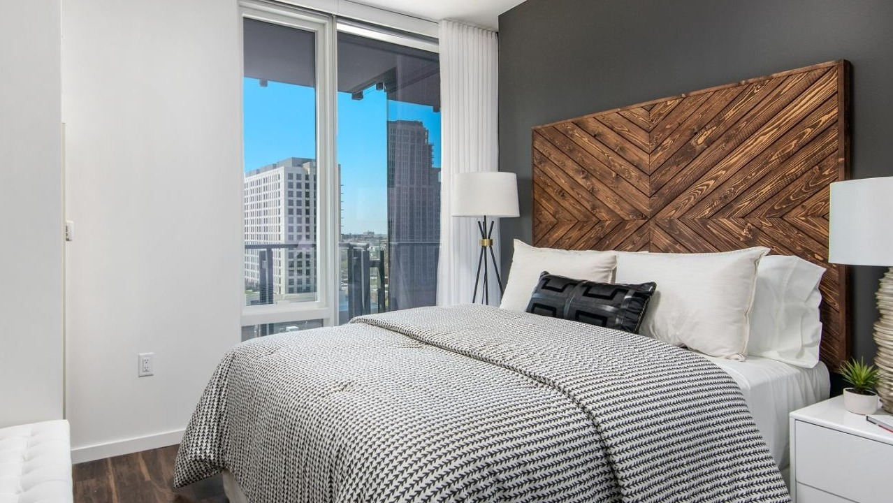 Stylish apartment bedroom with a unique wooden headboard, comfortable bedding, and large windows offering city views at Eleven40 in Chicago