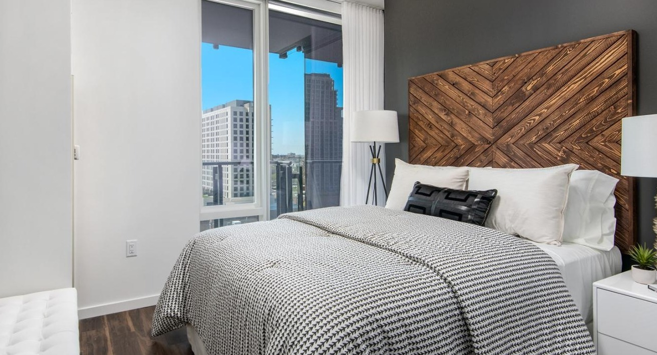Stylish apartment bedroom with a unique wooden headboard, comfortable bedding, and large windows offering city views at Eleven40 in Chicago