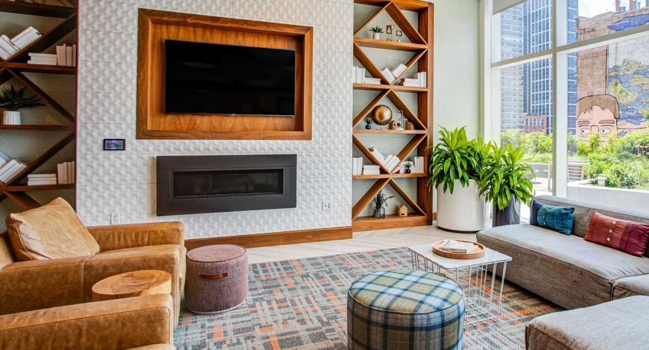 Cozy resident lounge with a fireplace, stylish built-in bookshelves, comfortable seating, and large windows at Eleven40 apartments in Chicago