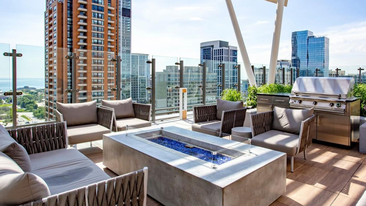Expansive rooftop lounge featuring a modern fire pit, comfortable seating, grilling stations, and city views at Eleven40 apartments in Chicago