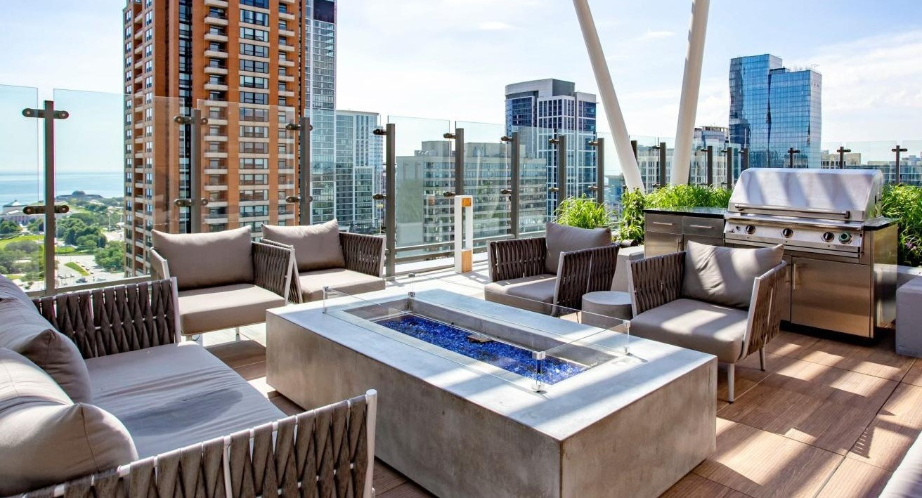 Expansive rooftop lounge featuring a modern fire pit, comfortable seating, grilling stations, and city views at Eleven40 apartments in Chicago